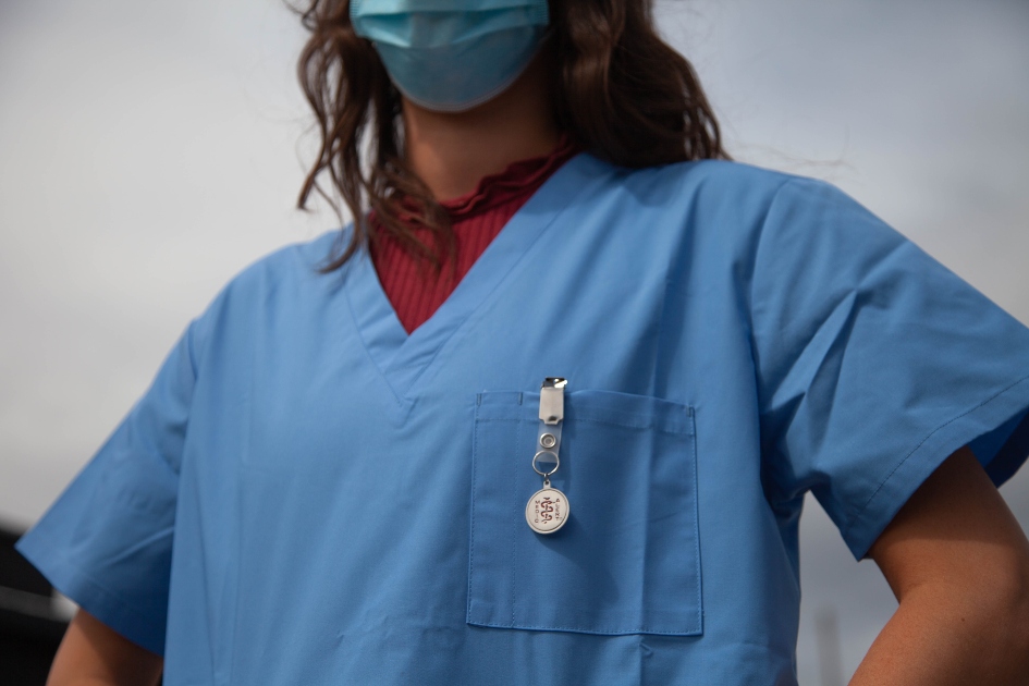 A woman nurse wearing blue scrubs and a mask